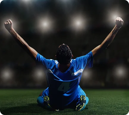 Un joueur de football en maillot bleu, numéro 4, est assis sur le terrain avec les bras levés triomphalement. Les lumières du stade illuminent la scène, créant une atmosphère de victoire.