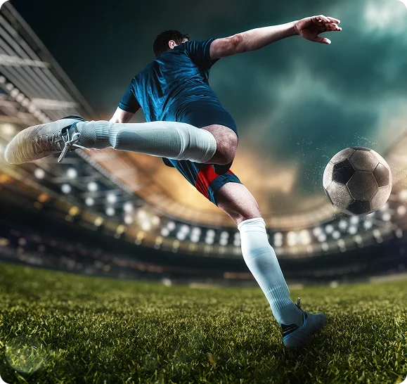 Un joueur de football en tenue bleue et rouge frappe un ballon en plein air dans un stade éclairé, transmettant intensité et concentration contre un ciel nuageux dramatique.